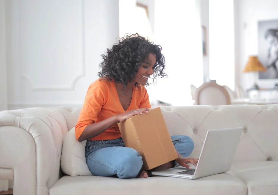 Persona abriendo un paquete junto a un portátil para ilustrar la experiencia de compra en ecommerce