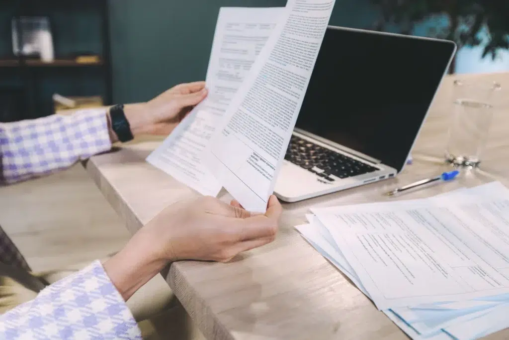 Persona revisando documentos junto a un portátil durante un proceso de verificación de información